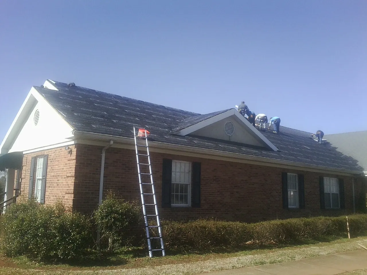 Crew tearing shingles off a brick ranch roof with a ladder set — Emergency Roof Repair work by our crew in Greenville
